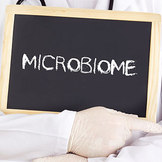 Doctor's hand holding chalk board with "Microbiome" written on it.