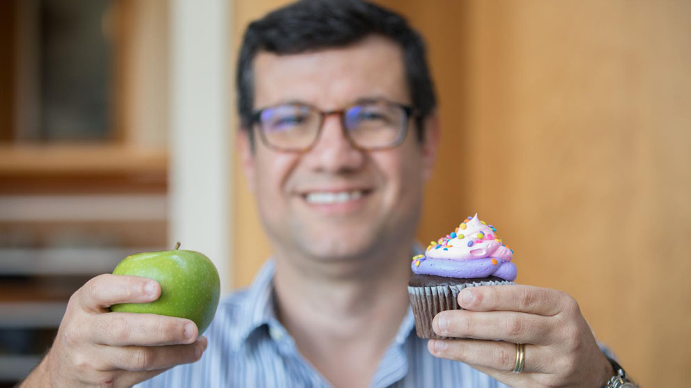 Mauro Costa, Ph.D. holding an apple and a cupcake.