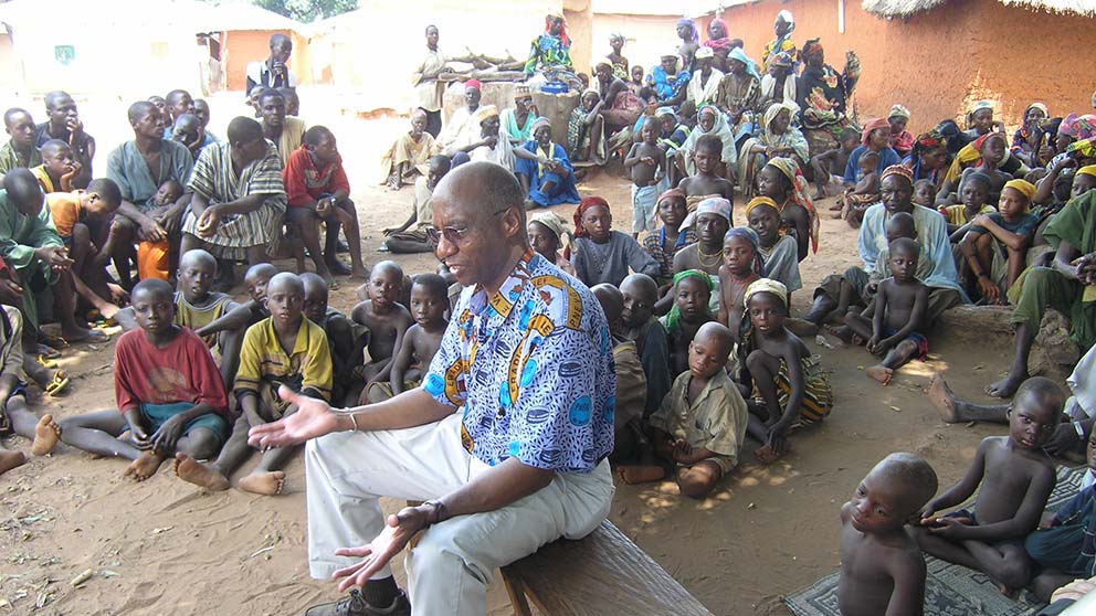 Caption: Hopkins speaks to a Nigerian village about Guinea worm prevention during a 2004 visit. The Carter Center/E. Staub
